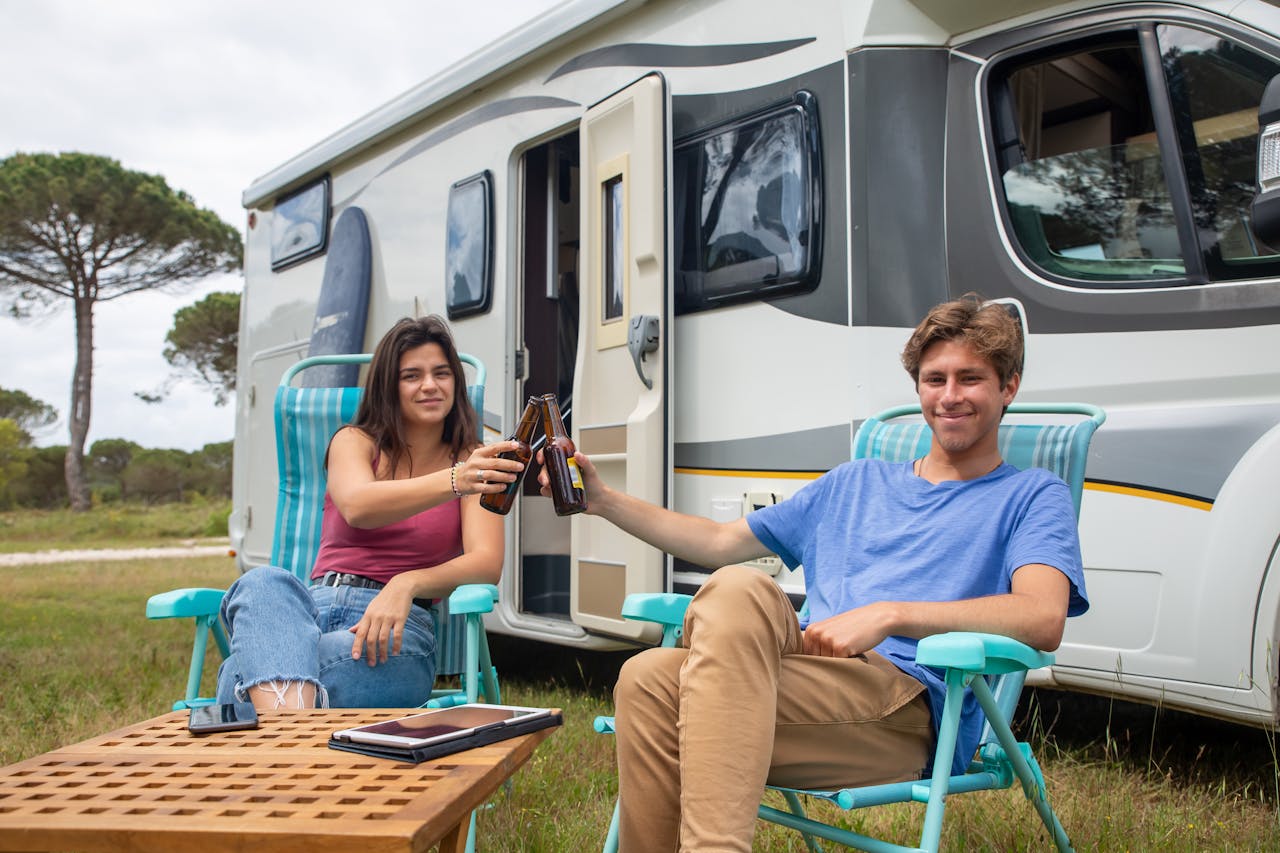 Happy couple clinking beer bottles outside camper during a relaxing vacation in Portugal.